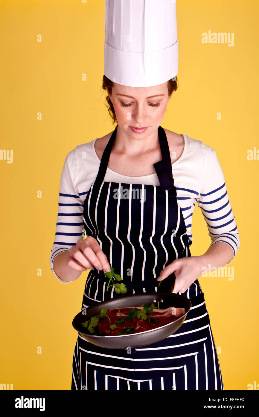 .Un giovane e attraente chef femmina tenendo un tegame con un bel pezzo di bistecca pronti per essere cucinati alla perfezione. Foto Stock