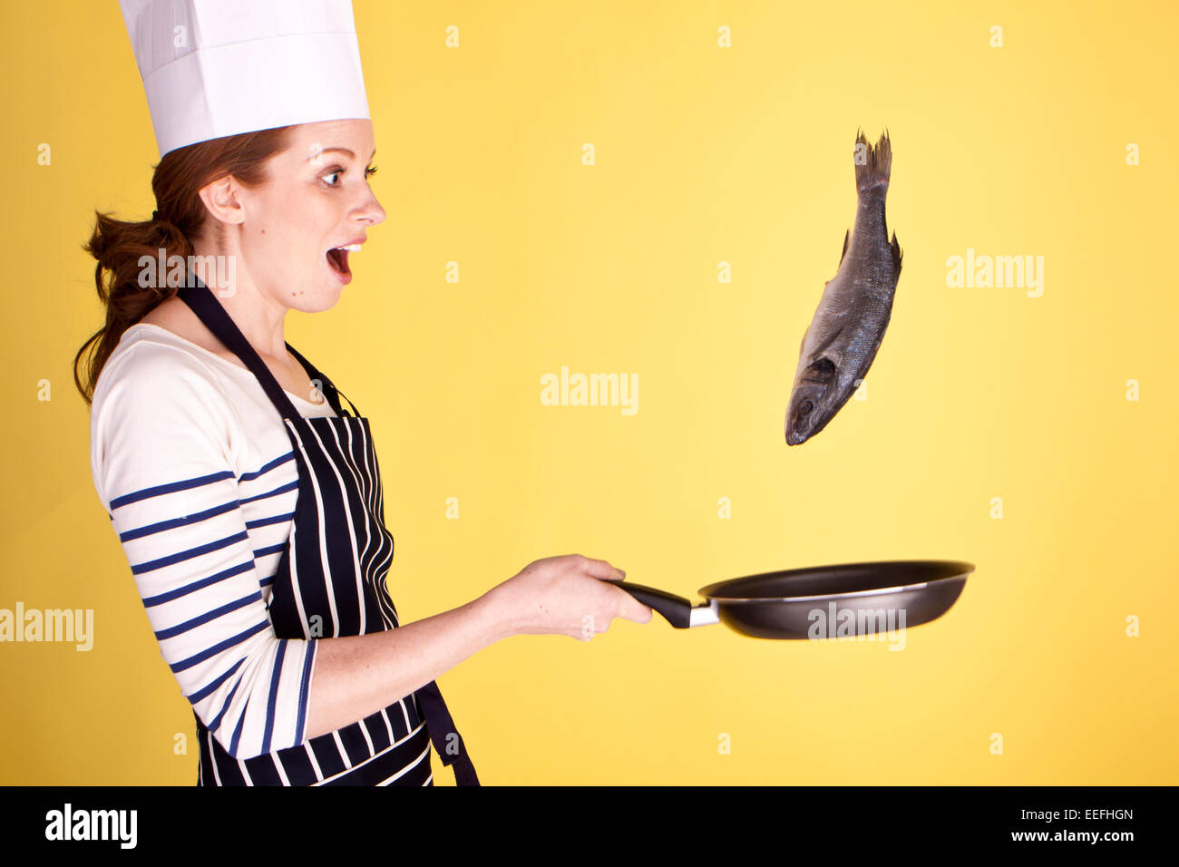 Un giovane attraente chef femmina capovolgimento di un pesce in una padella. Foto Stock