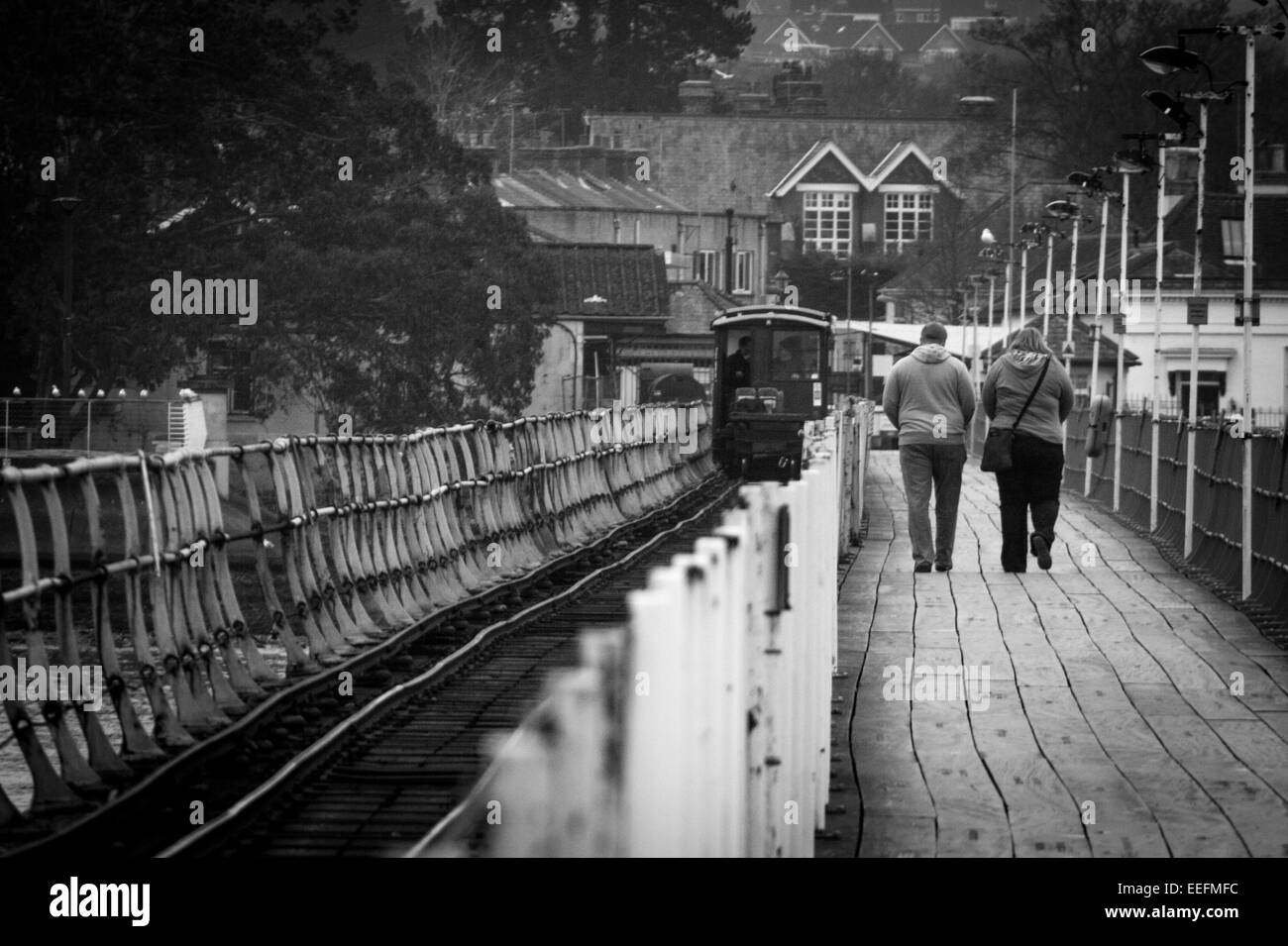 Giovane camminando lungo il molo di Hythe con un tram scendendo le piste accanto a loro. Foto Stock