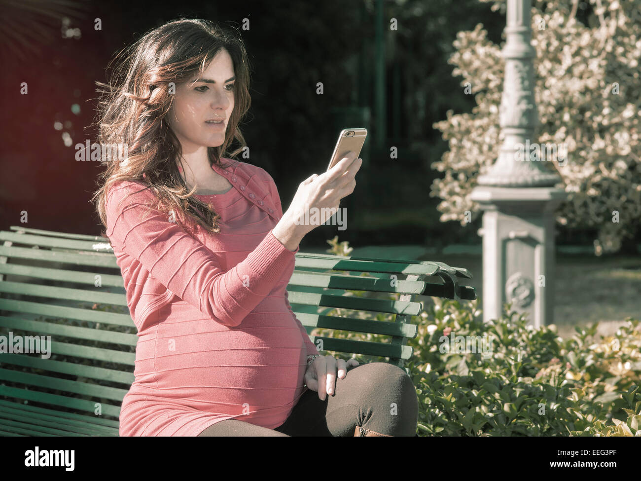 Una donna incinta con il suo portatile seduto in una sedia in un parco con stile istagram tonica Foto Stock