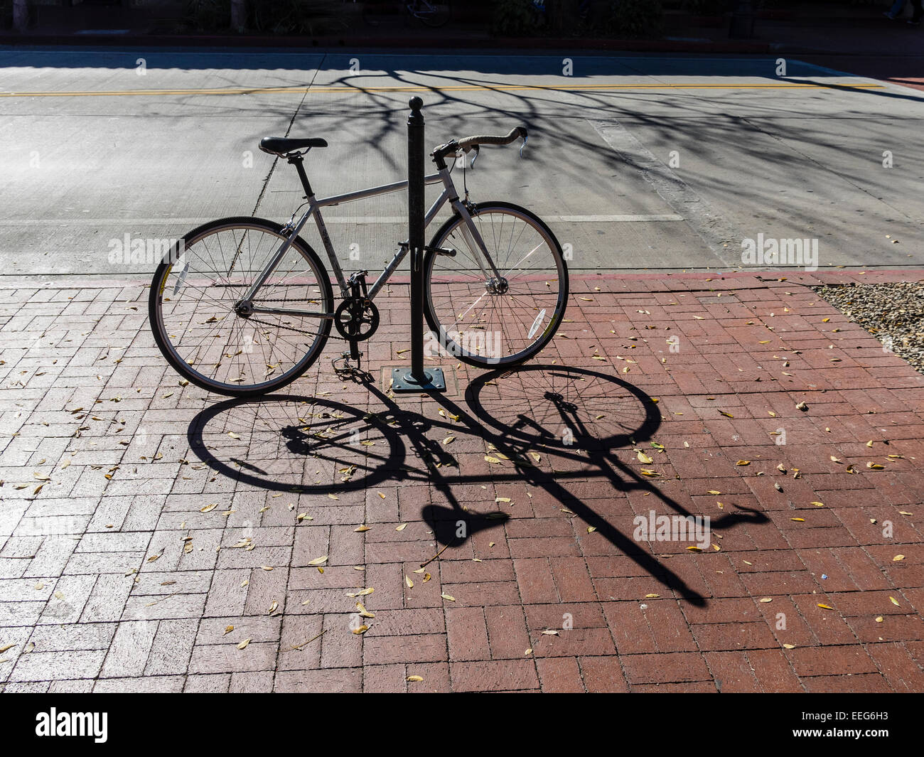 Una due ruote di bicicletta è parcheggiata e agganciato ad un palo su un marciapiede di mattoni su State Street a Santa Barbara, California. Foto Stock