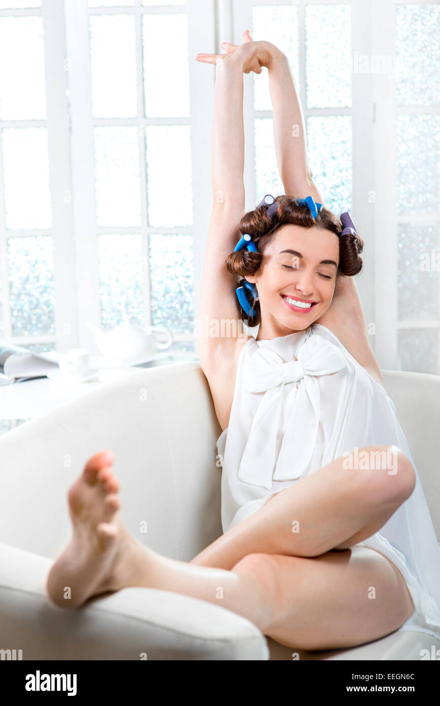 Giovane donna con bigodini in her hair sbadigliare e giacente nel lettino al bianco interni domestici Foto Stock