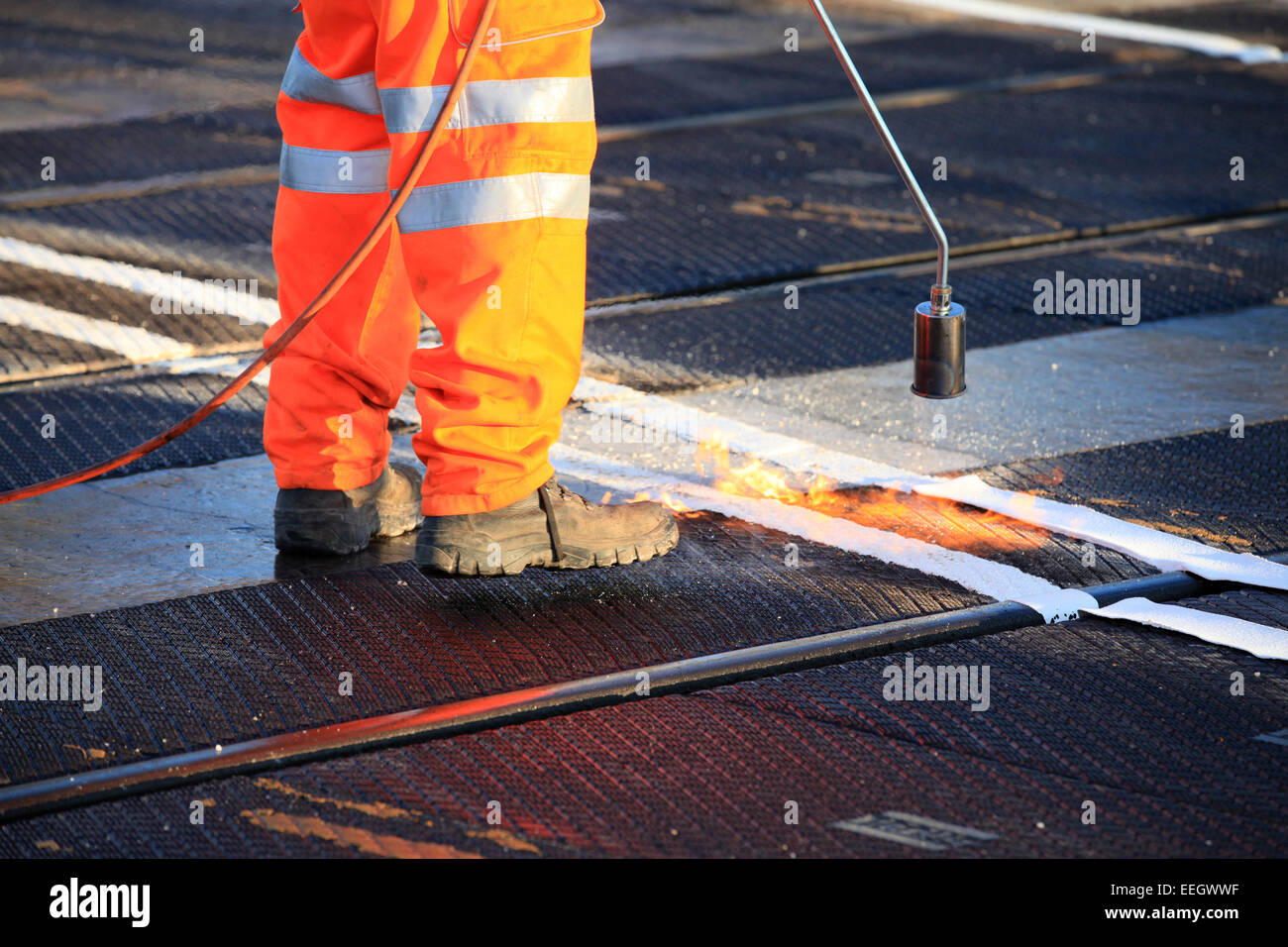 Salute e sicurezza, scarpe e indumenti ad elevata visibilità durante i lavori di riscaldare da inviare il materiale di rivestimento. Bruciatore a gas di gas propano. Foto Stock