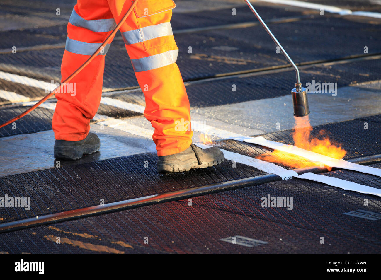 Salute e sicurezza, scarpe e indumenti ad elevata visibilità durante i lavori di riscaldare da inviare il materiale di rivestimento. Bruciatore a gas di gas propano. Foto Stock