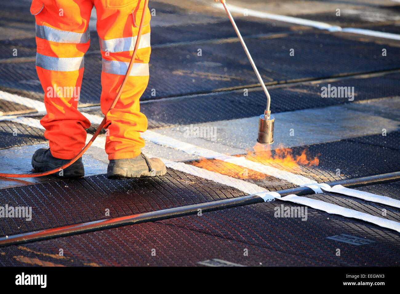 Salute e sicurezza, scarpe e indumenti ad elevata visibilità durante i lavori di riscaldare da inviare il materiale di rivestimento. Bruciatore a gas di gas propano. Foto Stock