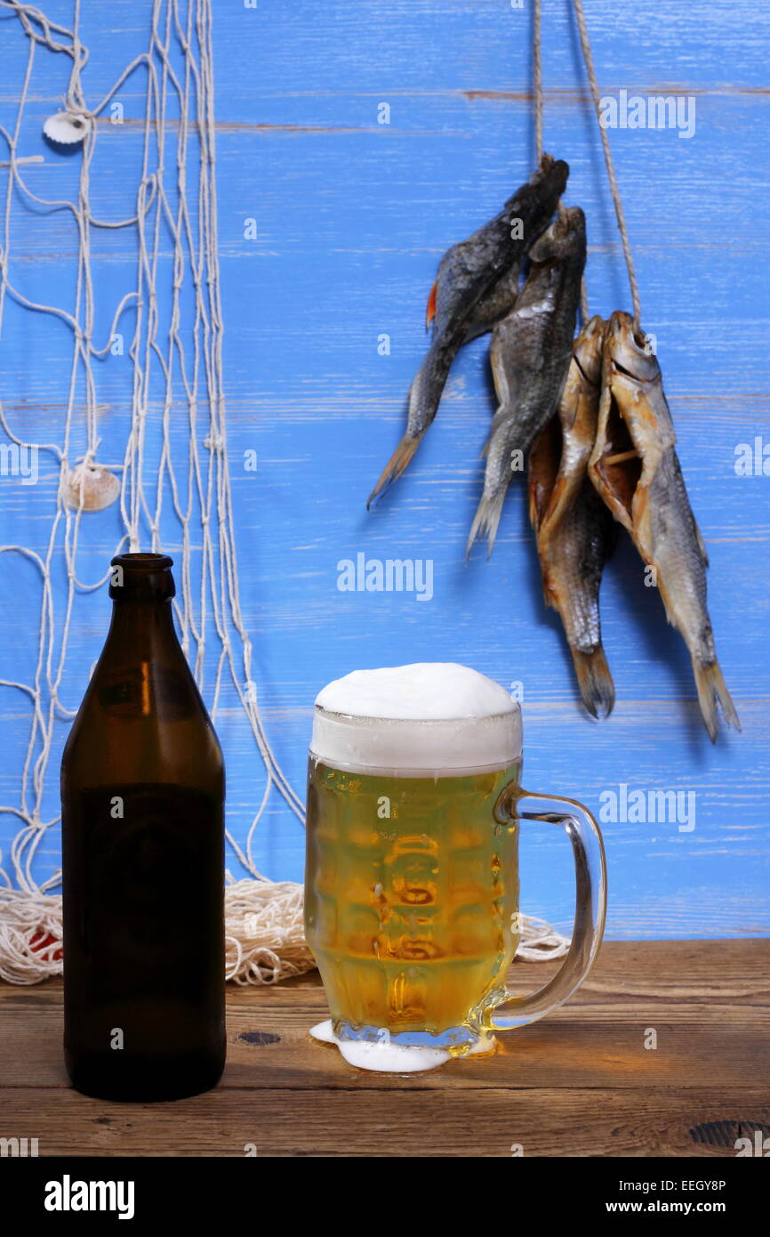 Boccale di birra su sfondo blu, essiccato rudd il pesce con la rete da pesca Foto Stock