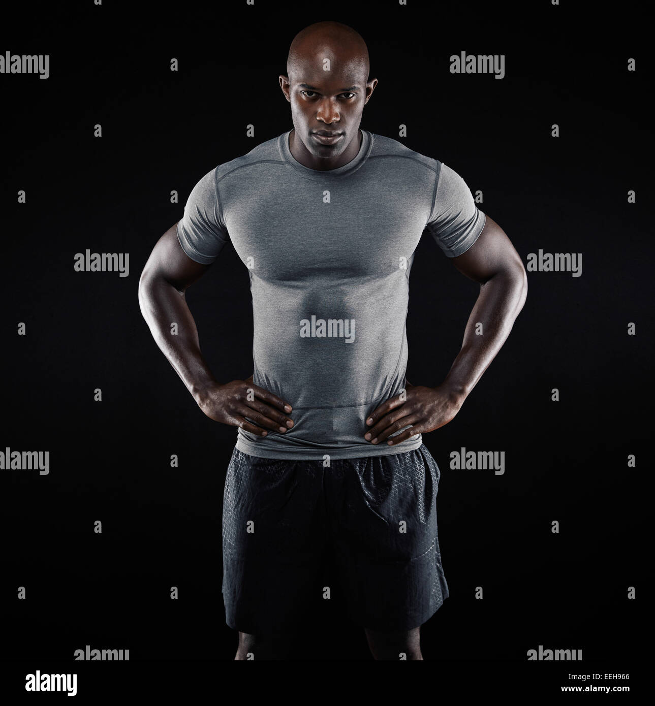 Ritratto di giovane muscolare uomo abbigliamento sportivo in piedi con le mani sui fianchi su sfondo nero. Forte atleta africana. Foto Stock