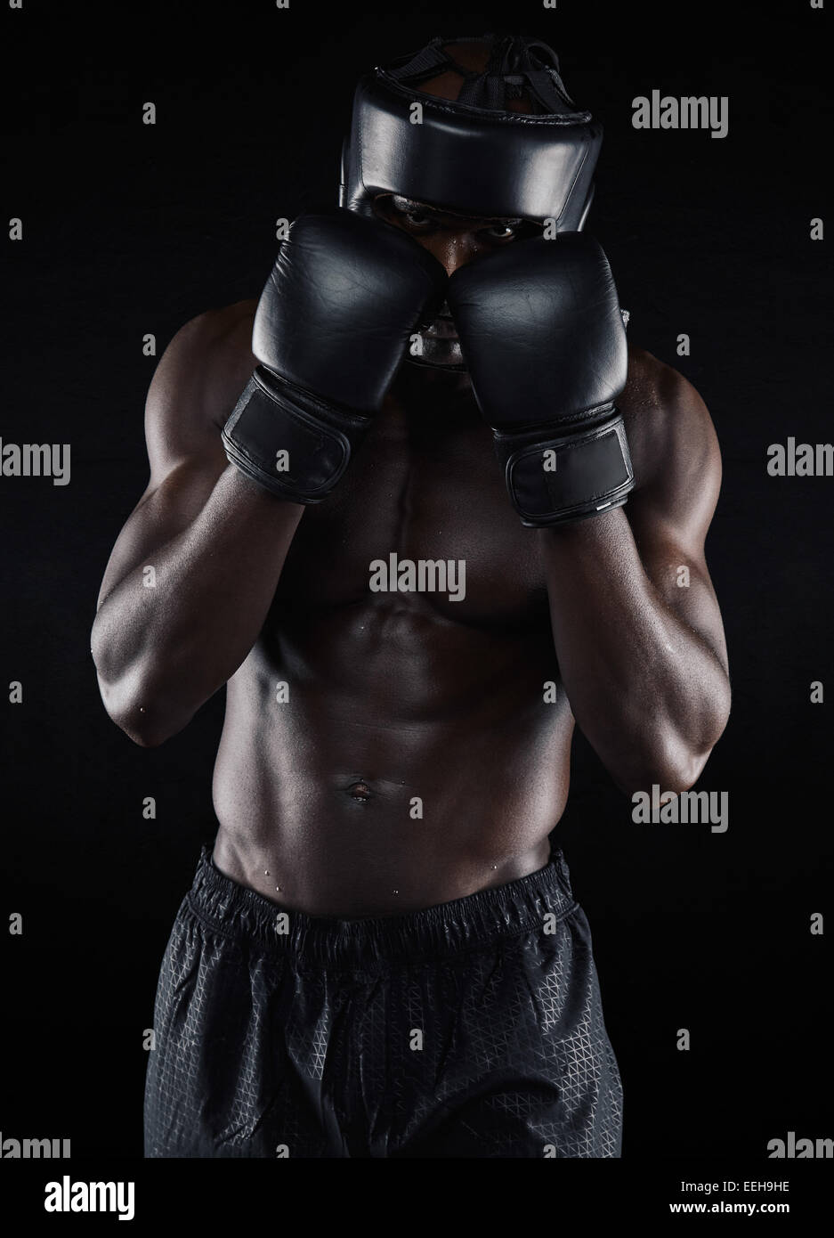 Ritratto di un giovane maschio boxer in un atteggiamento di combattimento su sfondo nero. Africa boxer maschio bloccando il suo volto con i guanti. Foto Stock