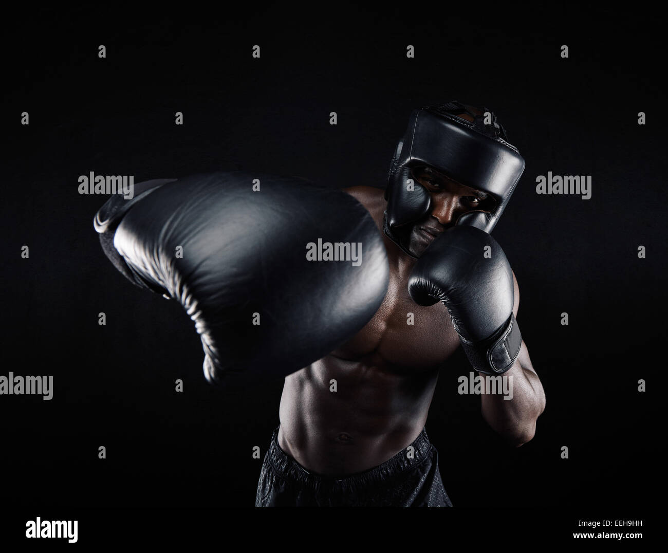 Ritratto del maschio africano praticare il pugilato su sfondo nero. Boxer maschio gettando un punzone di fronte. Giovane atleta. Foto Stock