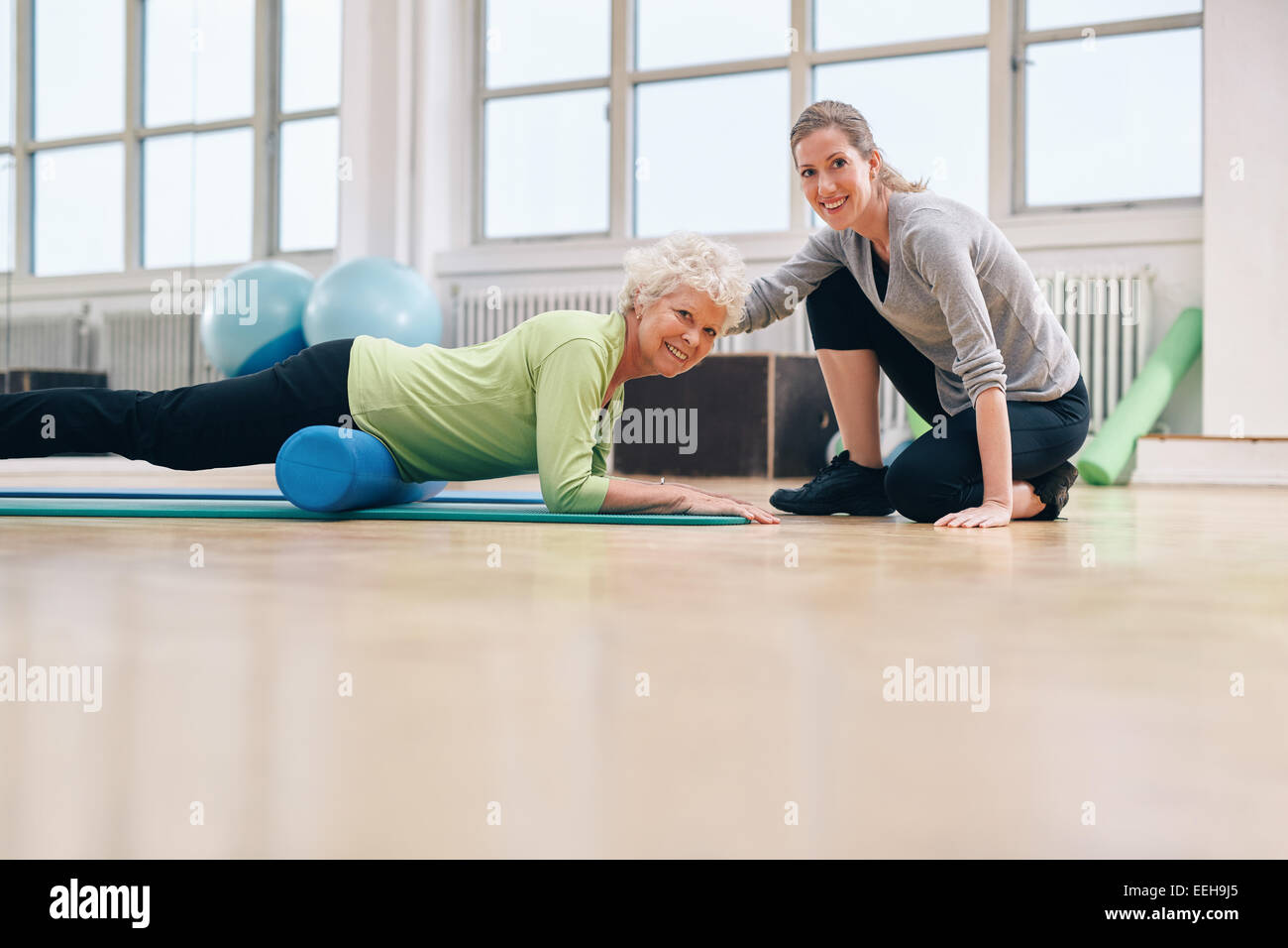 Donna anziana che fa esercizio su un rullo di schiuma con un personal trainer in palestra. allenatrice di palestra che aiuta una donna anziana nel suo allenamento a guarire Foto Stock