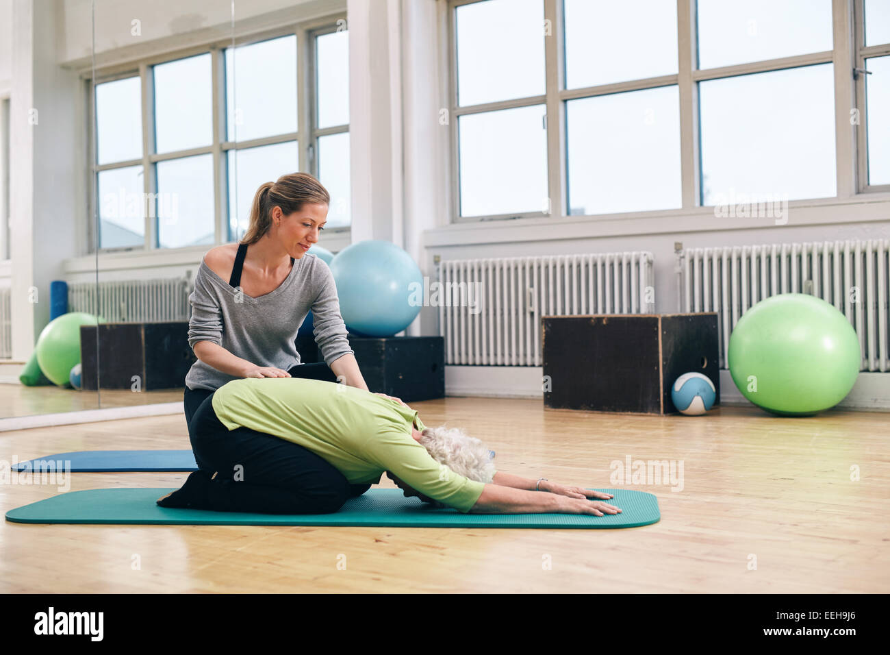 Trainer femminile aiutando senior donna fare yoga. Il sambuco donna china su di un tappeto di esercizio con istruttore personale contribuendo alla palestra. Foto Stock