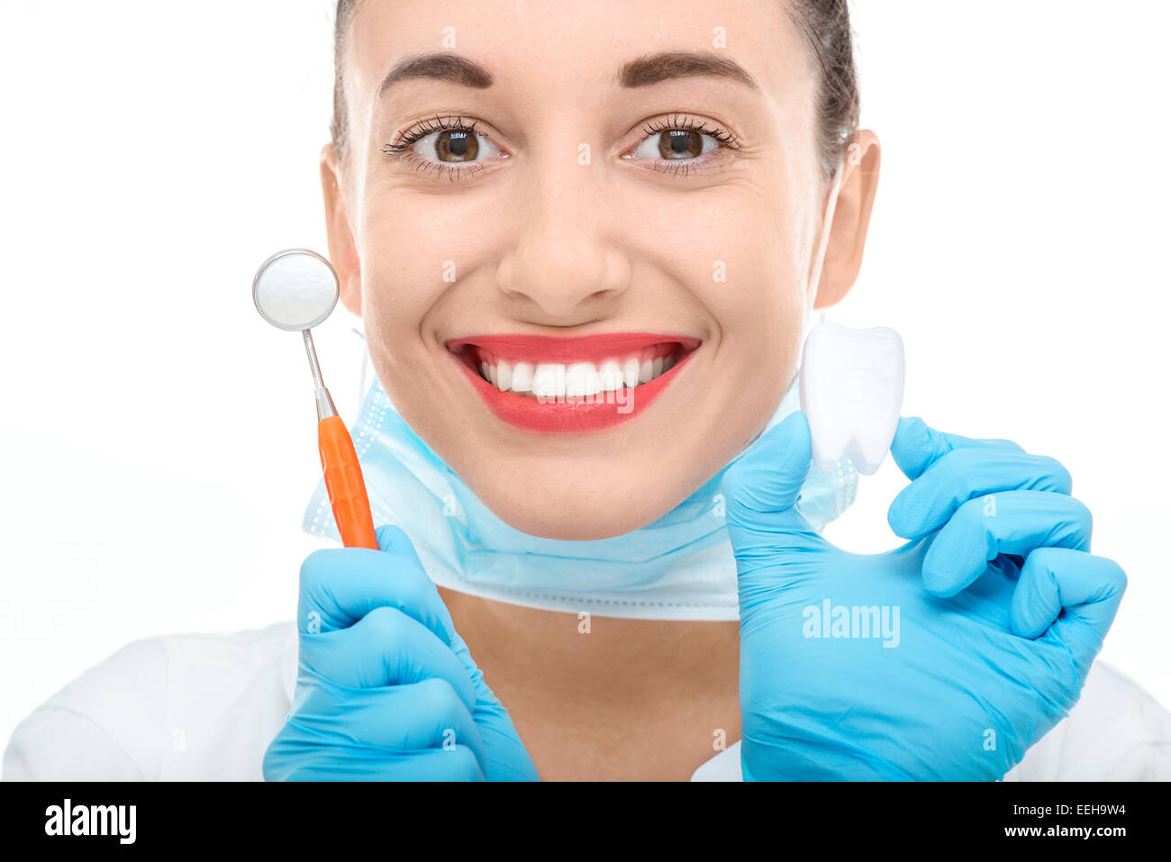 Giovane donna sorridente medico in uniforme tenendo lo specchio dentale e dente artificiale su sfondo bianco Foto Stock