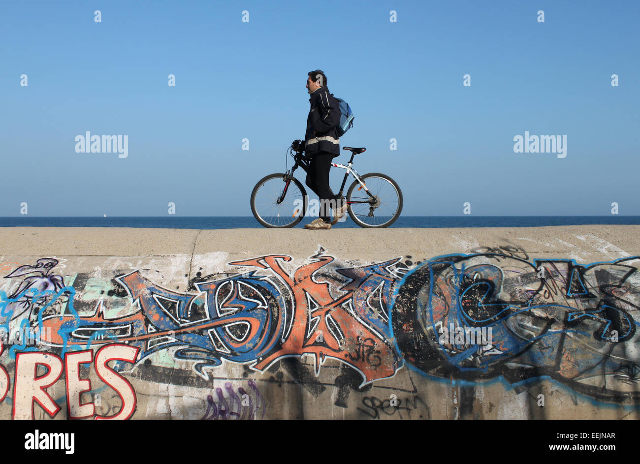 Uomo che cammina con la bici lungo coperto di graffiti parete accanto al mare, vicino a Badalona, Barcellona Foto Stock