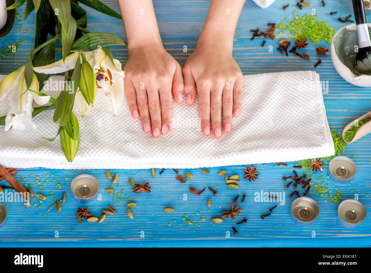 Donna prendendo cura delle sue mani sul telo da bagno in spa con fiori, candele e erbe blu sulla scrivania in legno Foto Stock