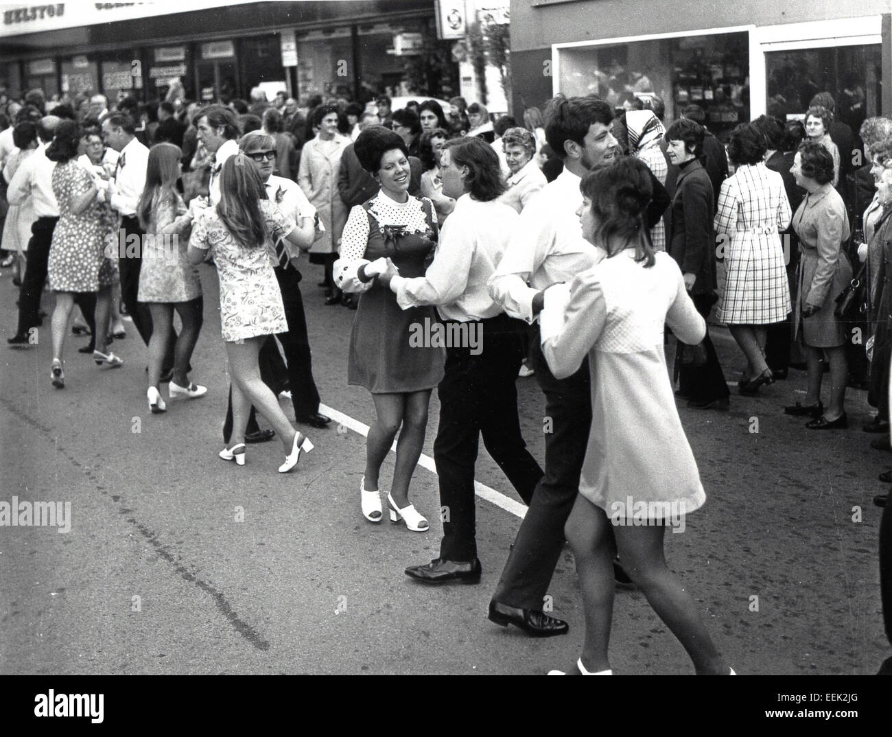 Anni '1960, storici, amanti dello shopping che guardano uomini e donne ballare insieme per strada, con ragazze che indossano abiti a motivi floreali e minigonne corte, Londra, Inghilterra. Forse Carnaby Street, il centro della moda britannica di quest'epoca. Foto Stock