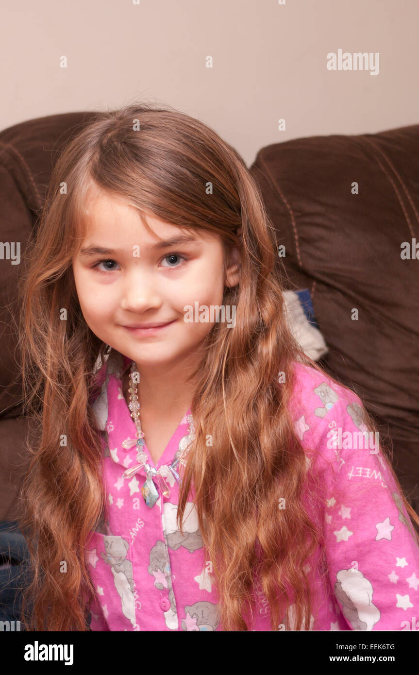 Bambina con capelli lunghi marrone sorridente guardando la telecamera indossando pigiami rosa Foto Stock