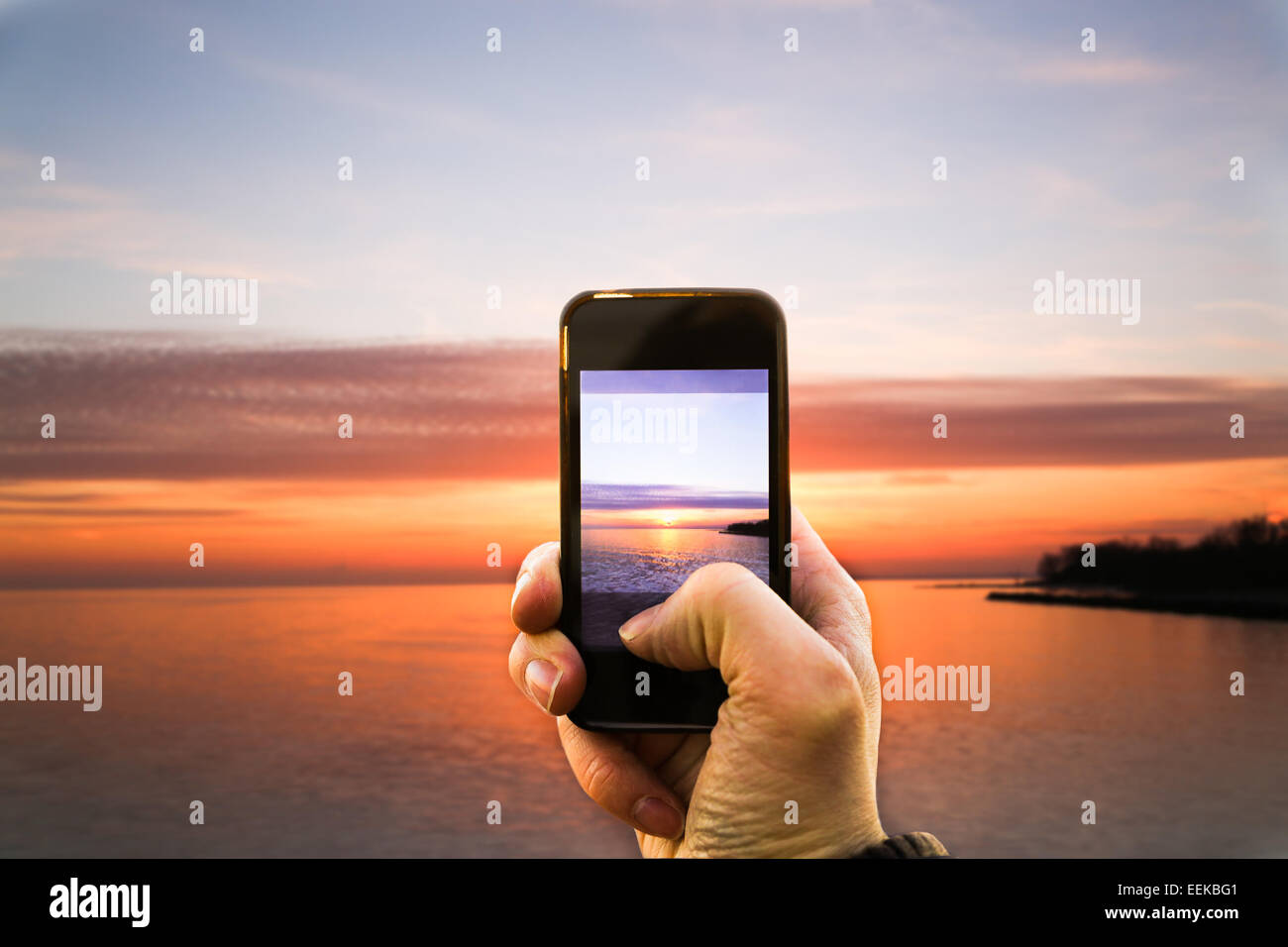 Una persona di scattare una foto di un tramonto con il proprio smartphone Foto Stock