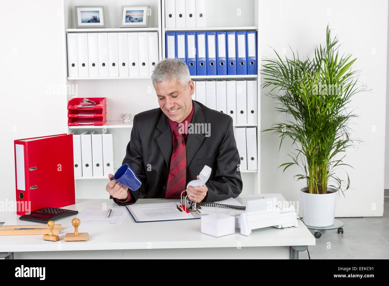 Mann mittleren altera sitzt im Büro am Schreibtisch mit leerer Tasse Kaffee in der mano, uomo di mezza età si siede in un ufficio Foto Stock