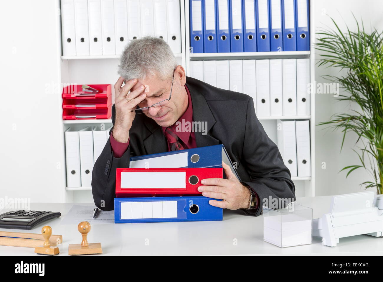 Mann mittleren altera sitzt im Büro, hält sich den Kopf, hat Kopfschmerzen, uomo di mezza età con un mal di testa, si siede nel suo ufficio, Foto Stock