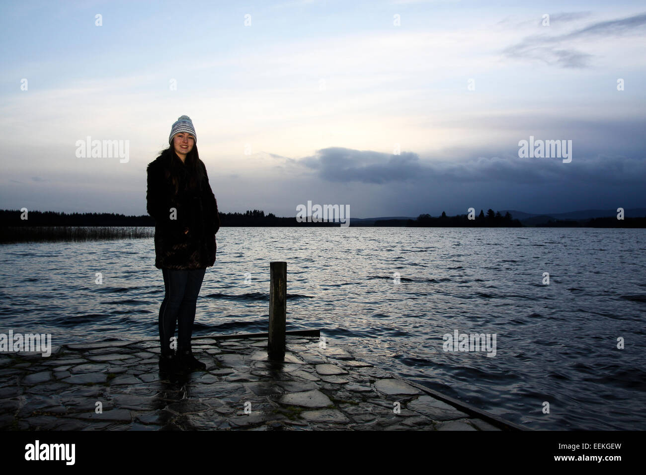 Giovane ragazza in piedi dal lago al crepuscolo Foto Stock