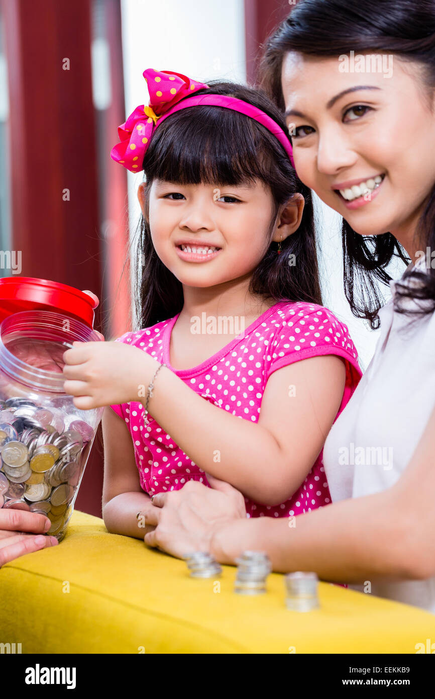 Famiglia cinese di risparmio di denaro per college fund del bambino, mettendo le monete in vaso Foto Stock