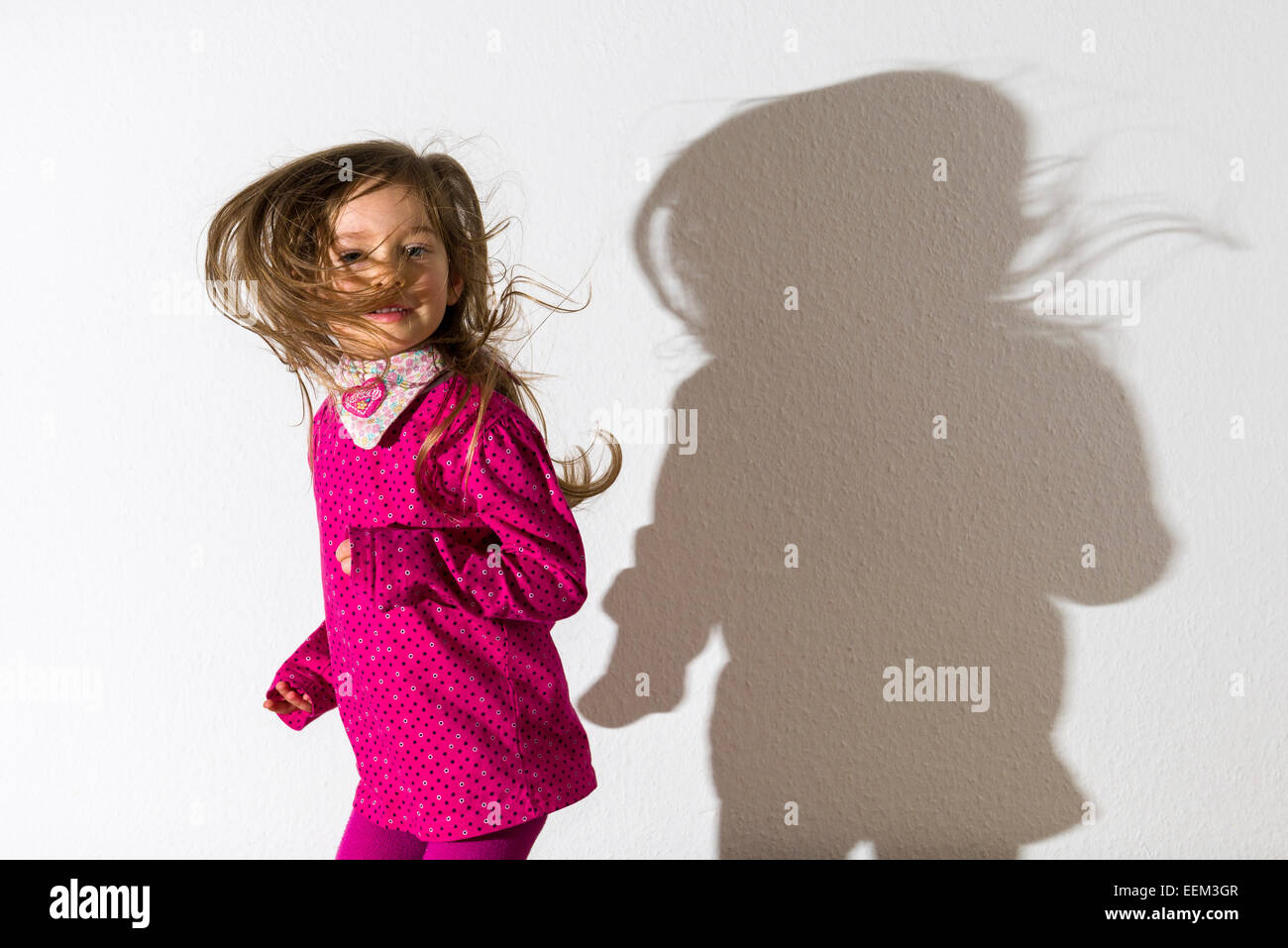 Ragazza 3 anni, indossa una camicia rosa, dancing, getta un' ombra su un muro bianco Foto Stock