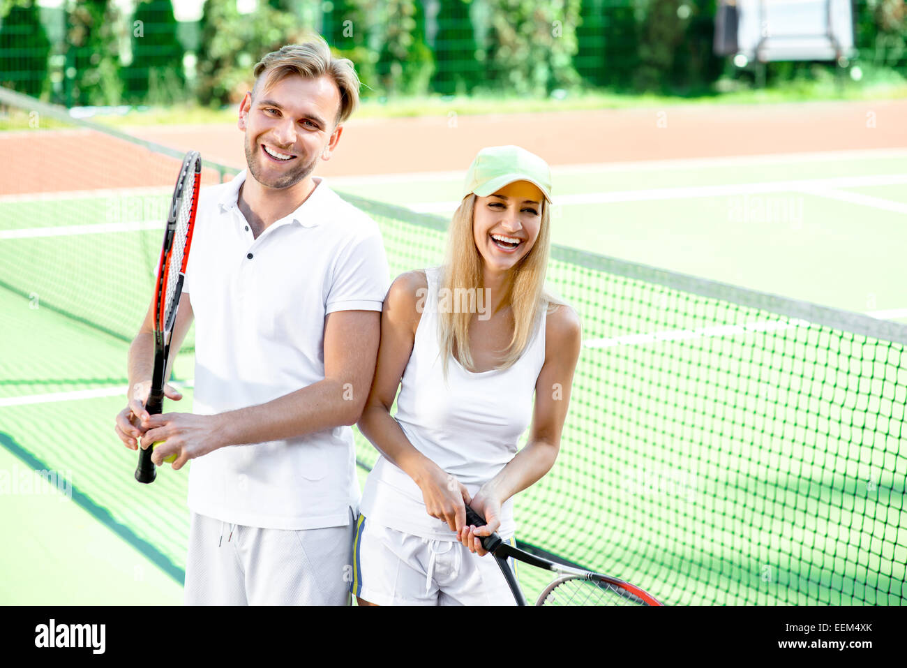 I giovani coniugi giocando a tennis in bianco sportwear sul campo da tennis esterno in estate Foto Stock