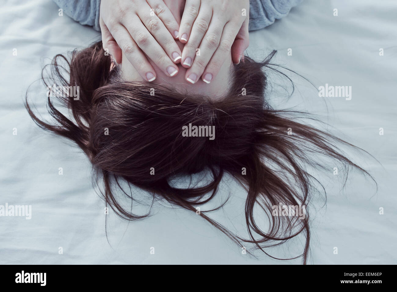 Donna sdraiata sul letto che copre la sua gli occhi con le mani Foto Stock