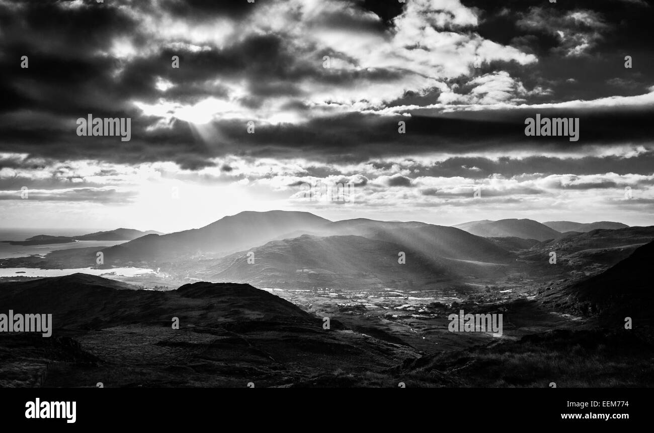 L'Irlanda, nella contea di Cork, Adrigole, piercing raggi di sole attraverso le nubi sul villaggio nella valle di montagna Foto Stock