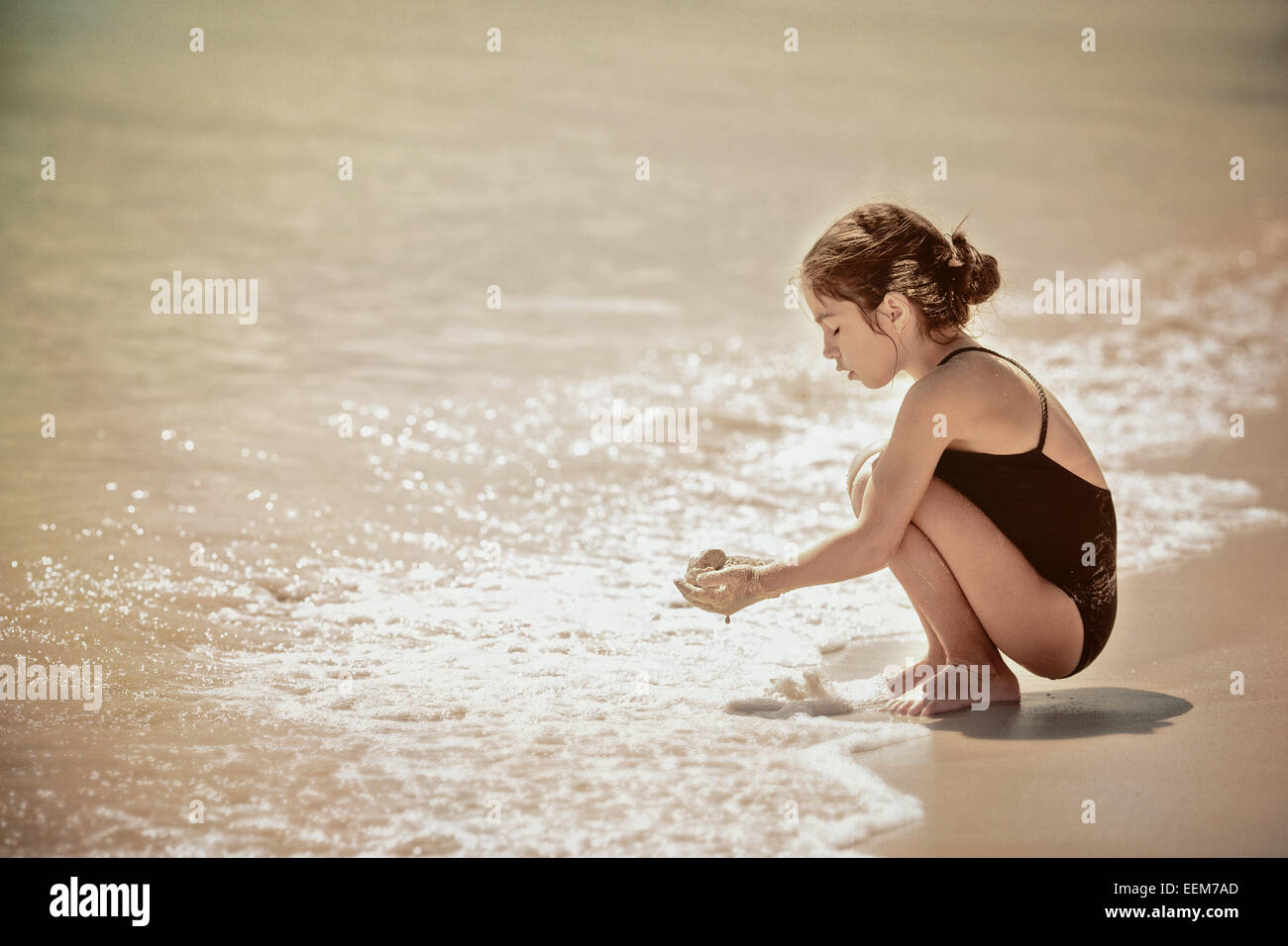 Ragazza accovacciato dal bordo d'acqua sulla spiaggia sabbiosa e tenere sabbia bagnata in mani Foto Stock