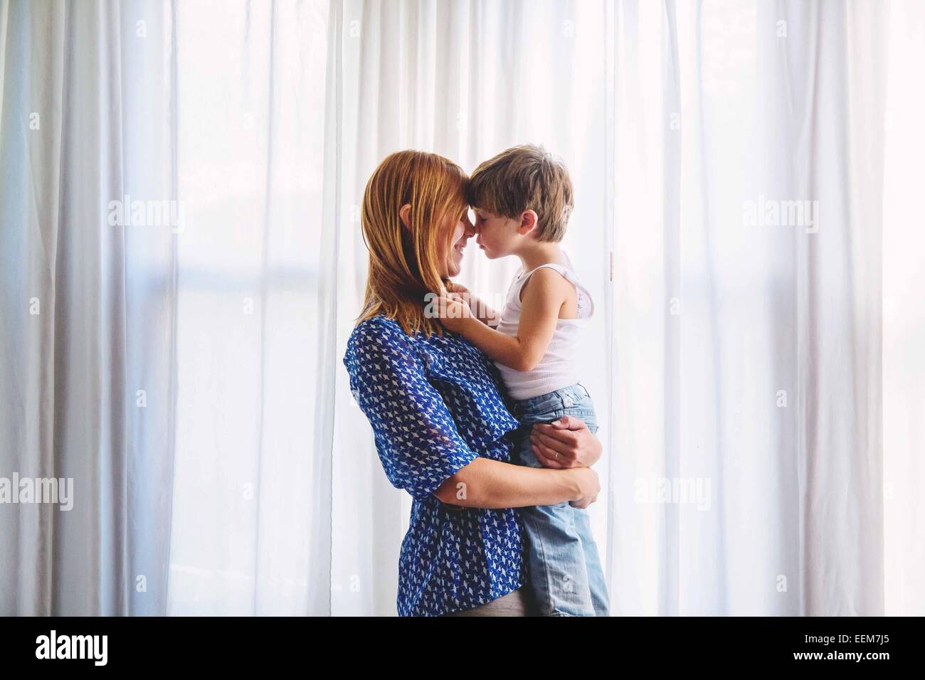 Madre e figlio faccia a faccia vicino a una finestra Foto Stock