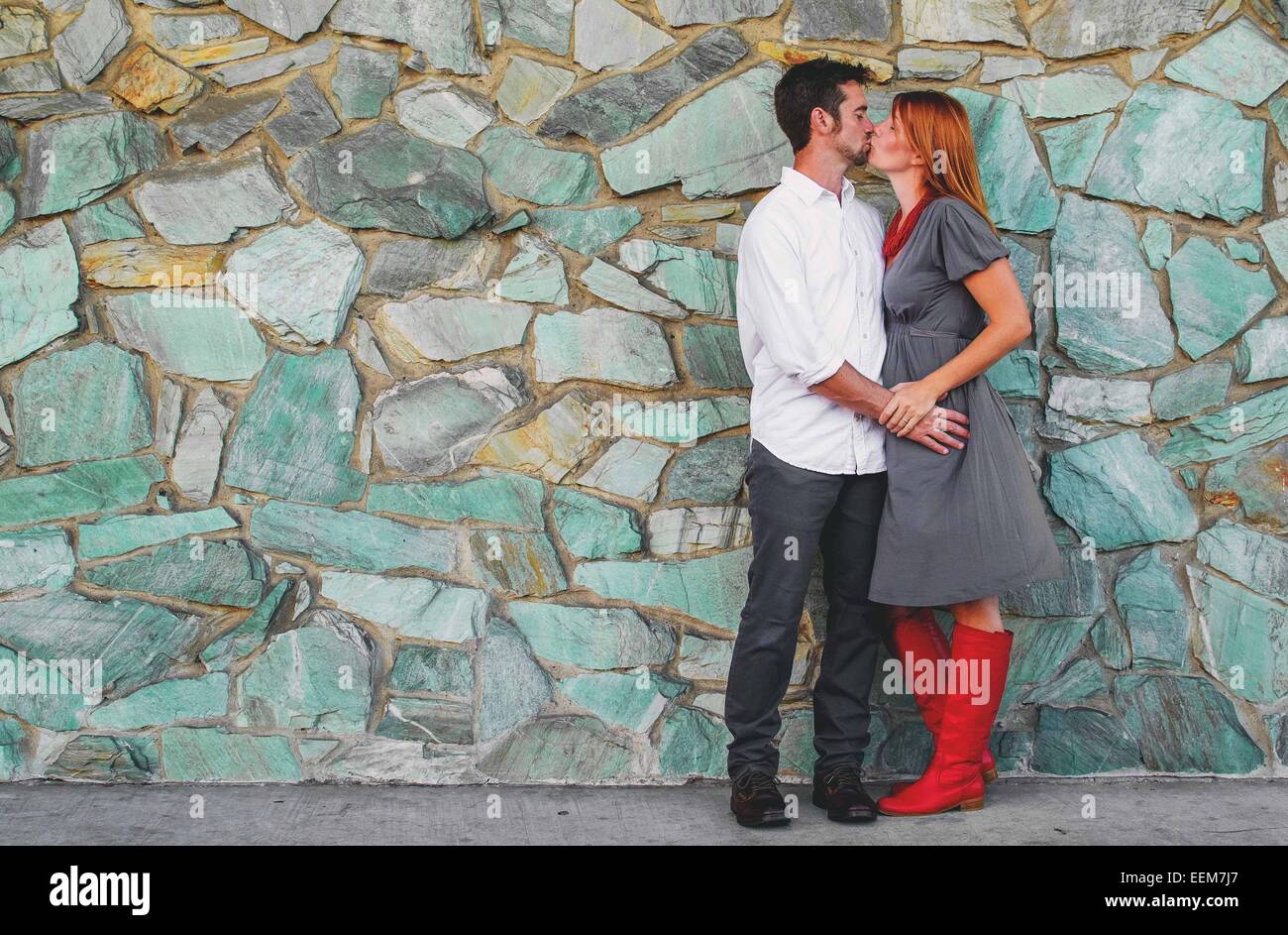 Coppia in piedi da un muro di pietra baciando Foto Stock