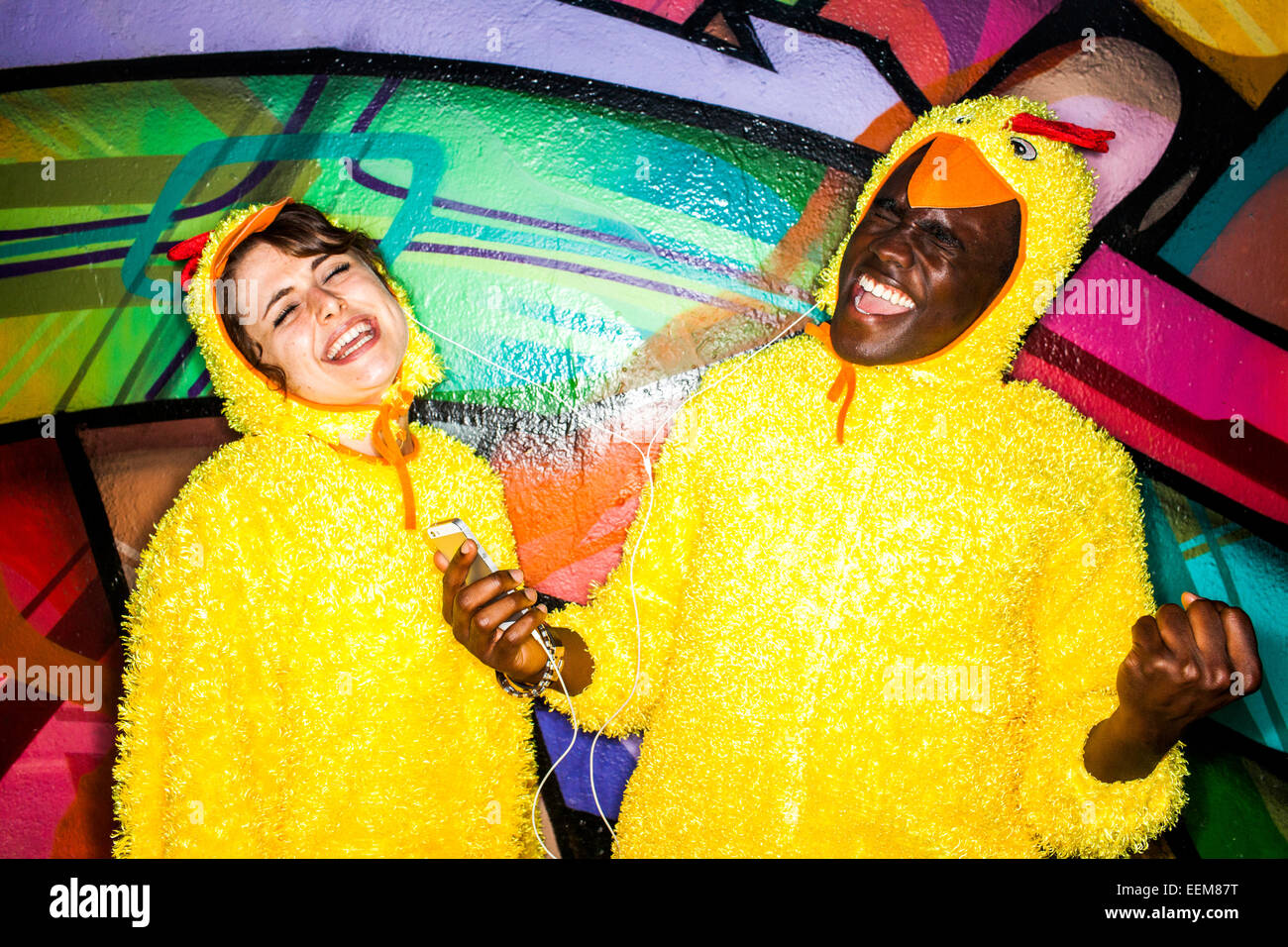 Matura in costumi identici ascoltando gli auricolari vicino al muro di graffiti Foto Stock