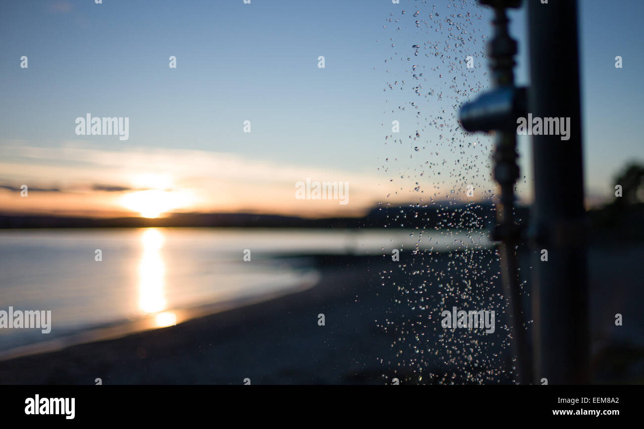 Close up di acqua che cade dalla doccia sulla spiaggia durante il tramonto Foto Stock