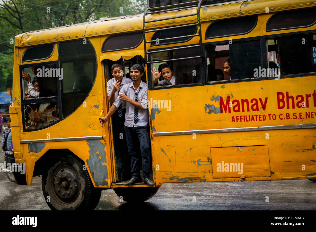 Studenti che fanno il tifo fuori dalla porta di ingresso di un autobus scolastico che si muove su una strada trafficata a Bodh Gaya, Bihar, India. Foto Stock