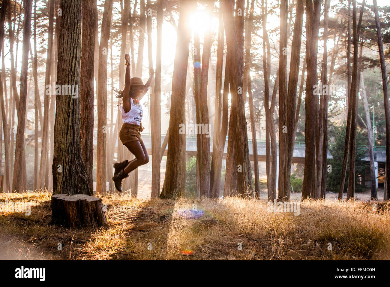 Nero donna jumping dal moncone nella foresta di sole Foto Stock