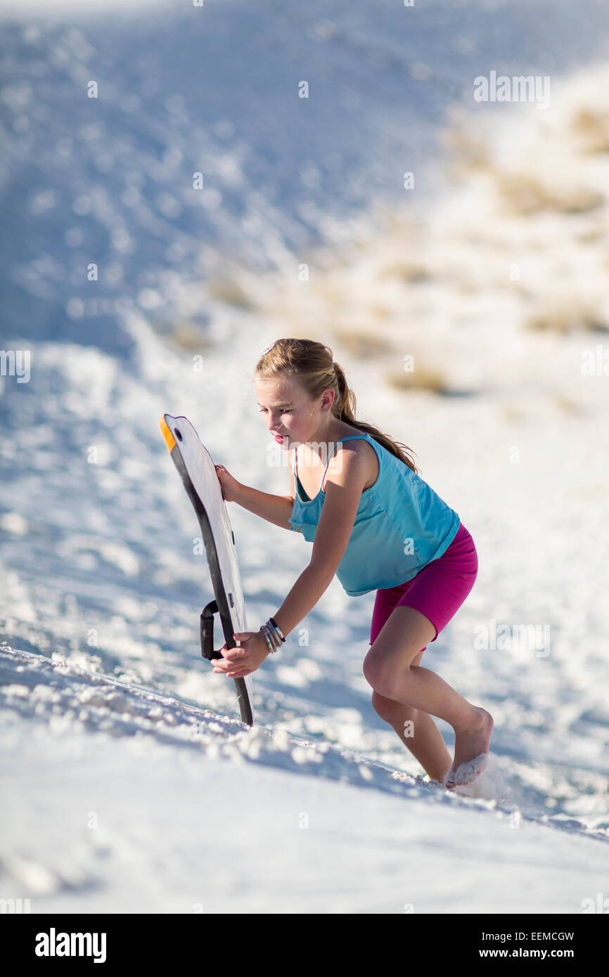 Ragazza caucasica climbing duna di sabbia con slitta Foto Stock