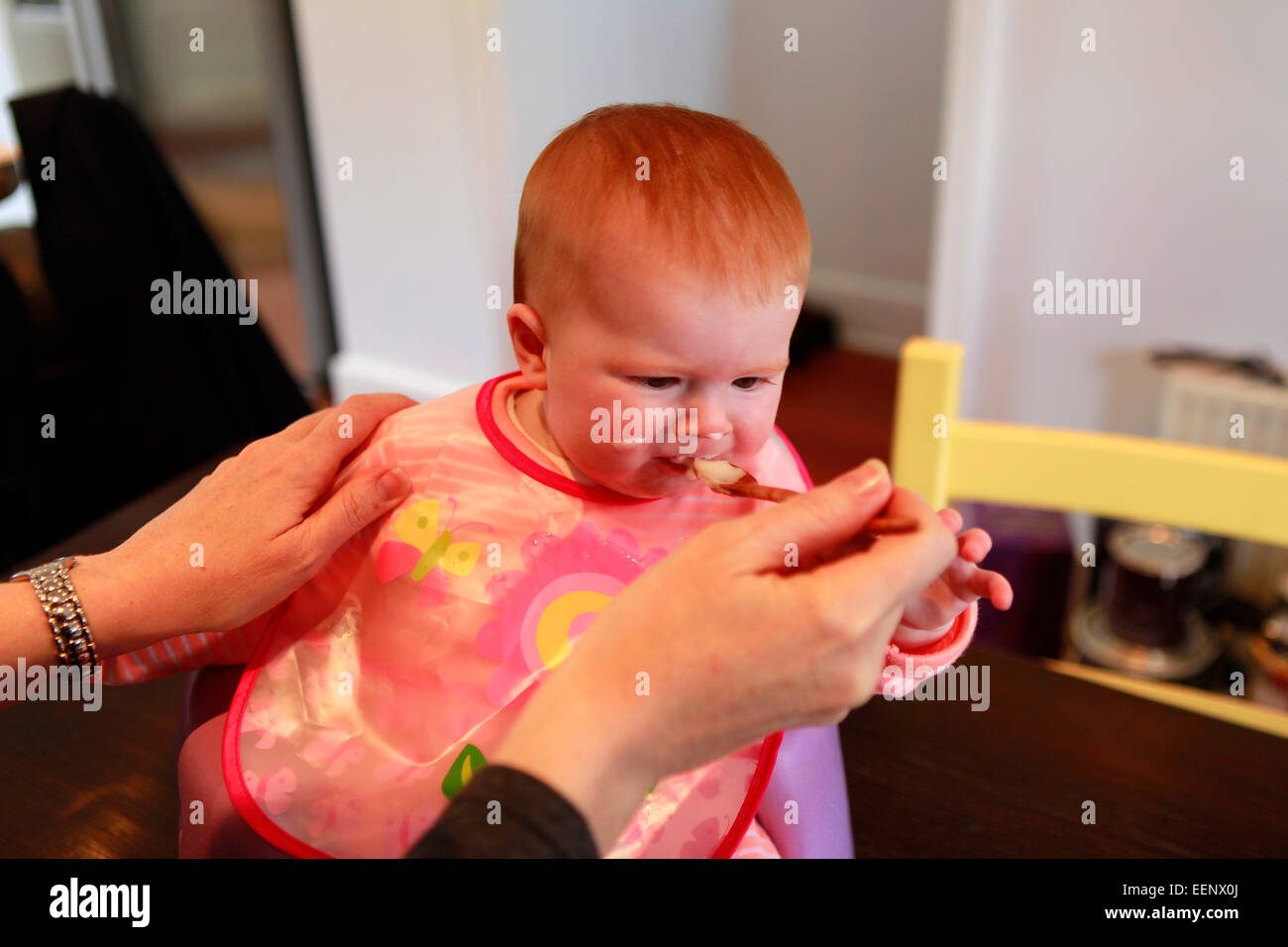 Sei mesi dai capelli rossi ragazza bambino essendo alimentato cibo solido per la prima volta da sua madre Foto Stock