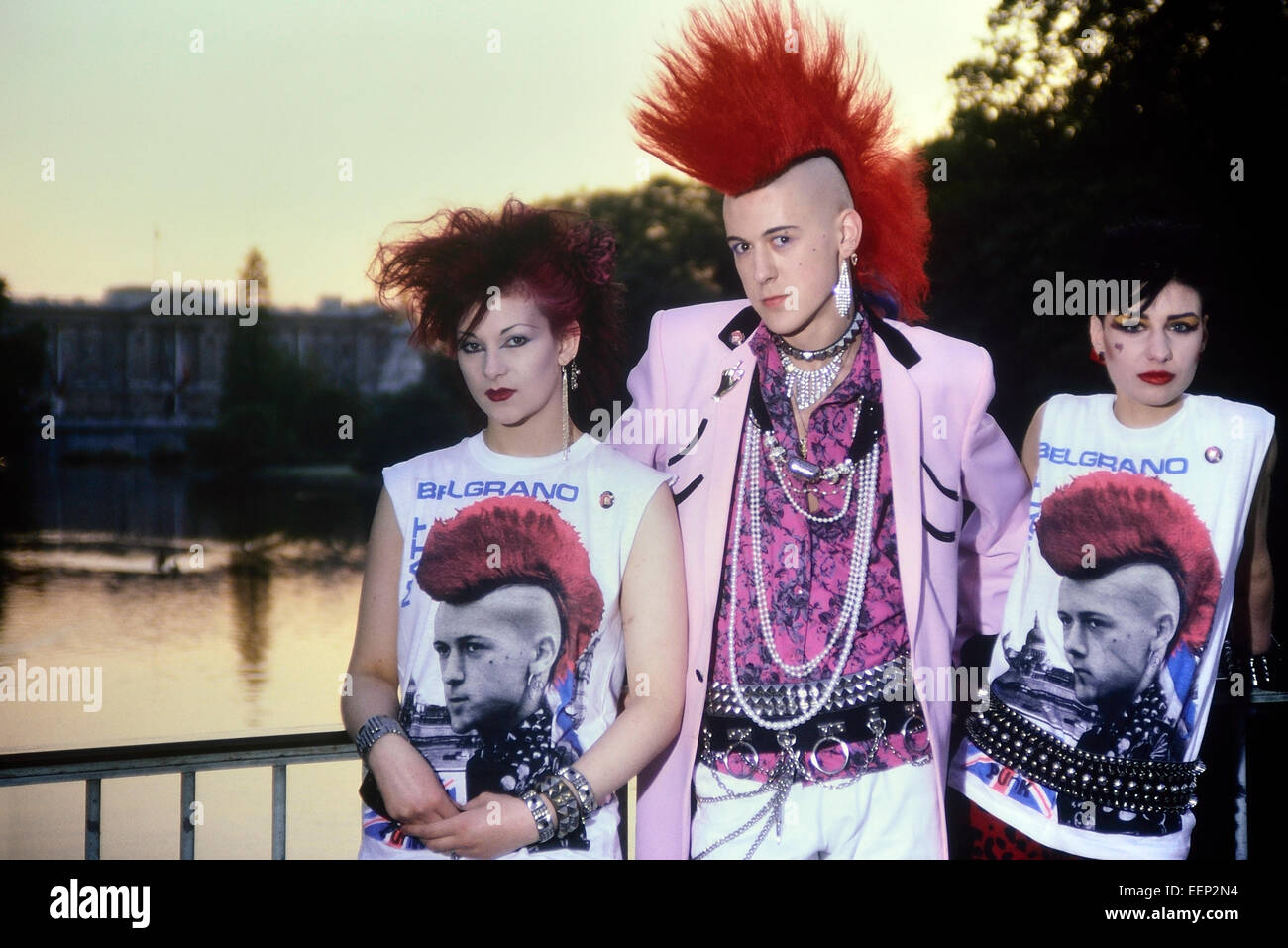 'Punk da cartolina' Matt Belgrano che indossa una giacca di colza Teddy Boy rosa, in posa con due punk femmina fuori da Buckingham Palace. Londra. Circa anni '80 Foto Stock