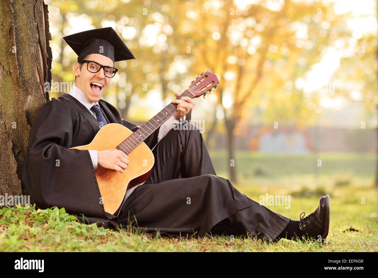 Studente laureato suonare la chitarra acustica in posizione di parcheggio Foto Stock