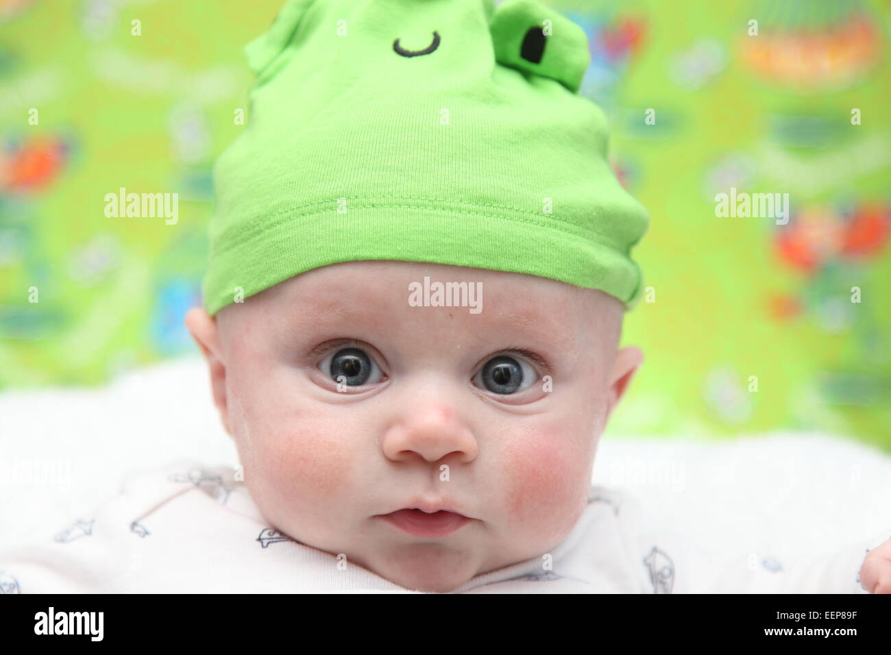 Blue eyed Caucasian baby boy indossando una rana verde hat Foto Stock
