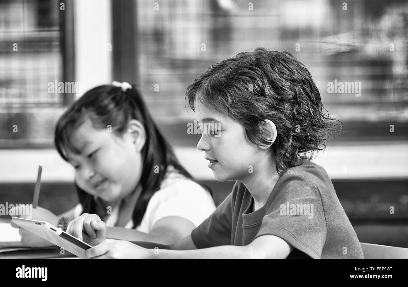 Due bambini multirace utilizzando tablet e il disegno con matite a scuola. Il concetto di istruzione. Foto Stock