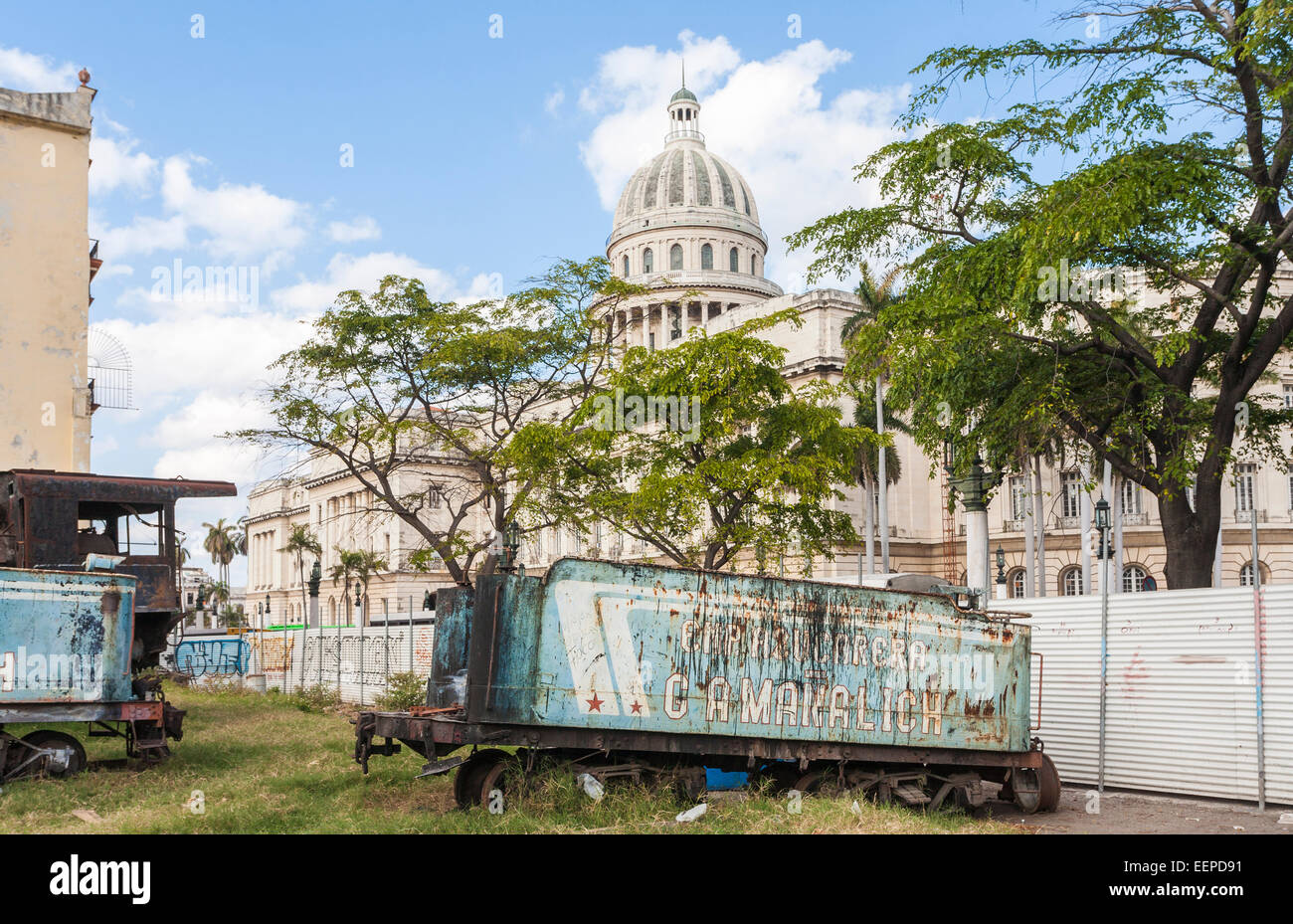 Vista della cupola della mitica nazionale di Capitol Building, Old Havana, Cuba dietro un derelitti, arrugginito treno offerta in un centro urbano scrapyard Foto Stock