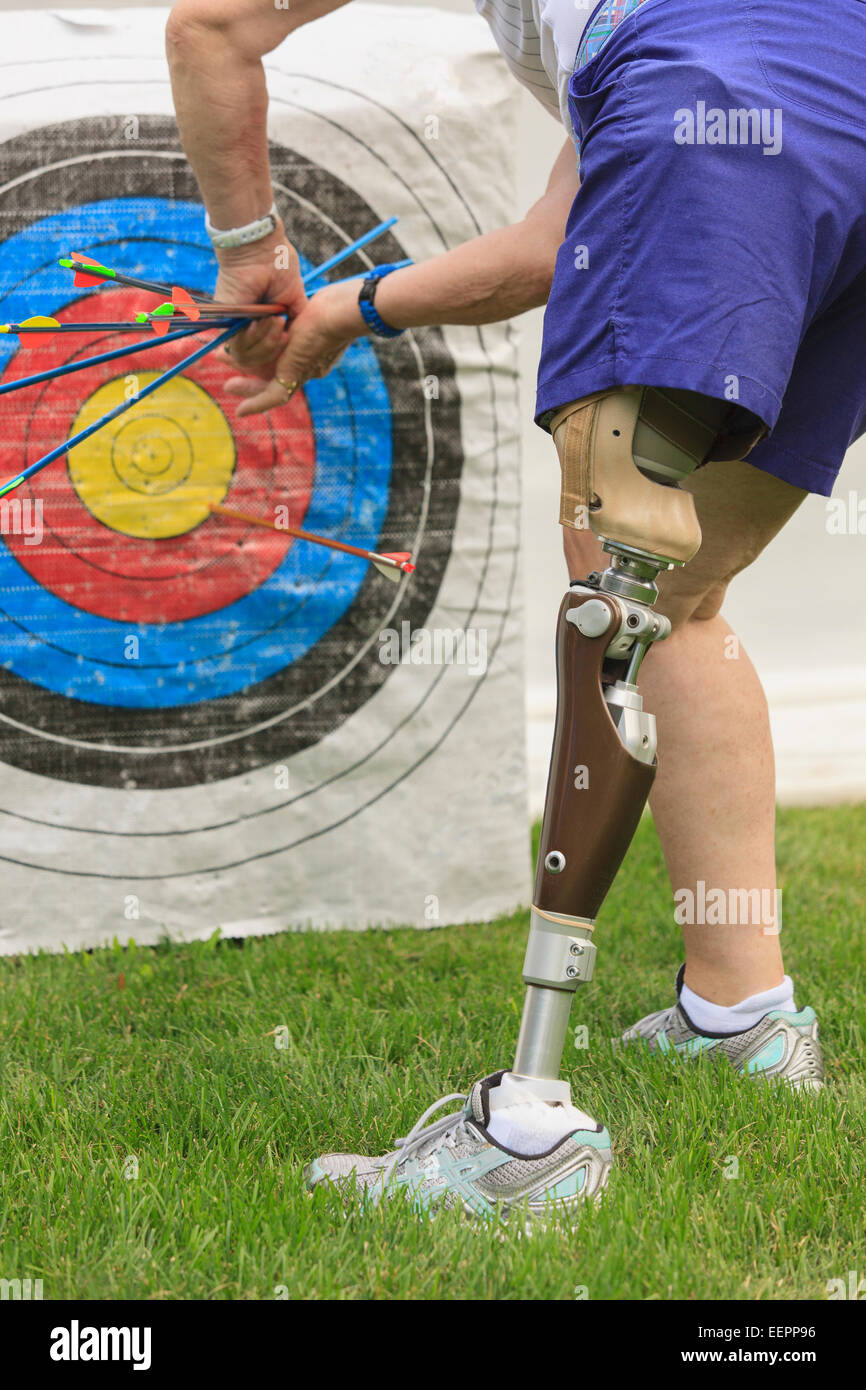 Donna con gamba protesico tirando le frecce dal bersaglio dopo la pratica di tiro con l'arco Foto Stock
