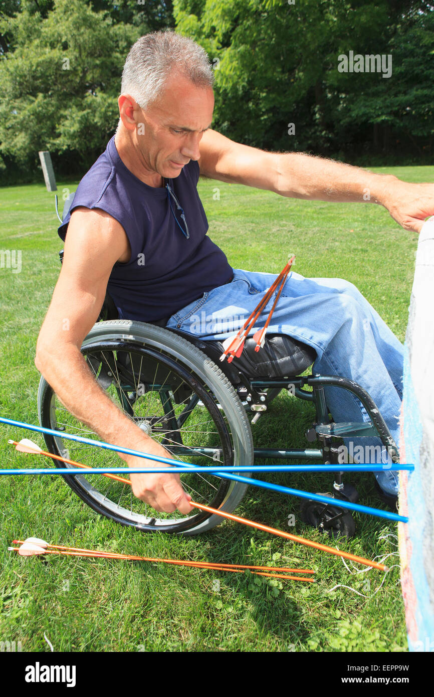 Uomo con lesioni al midollo spinale in carrozzella rimozione frecce dal bersaglio dopo la pratica di tiro con l'arco Foto Stock