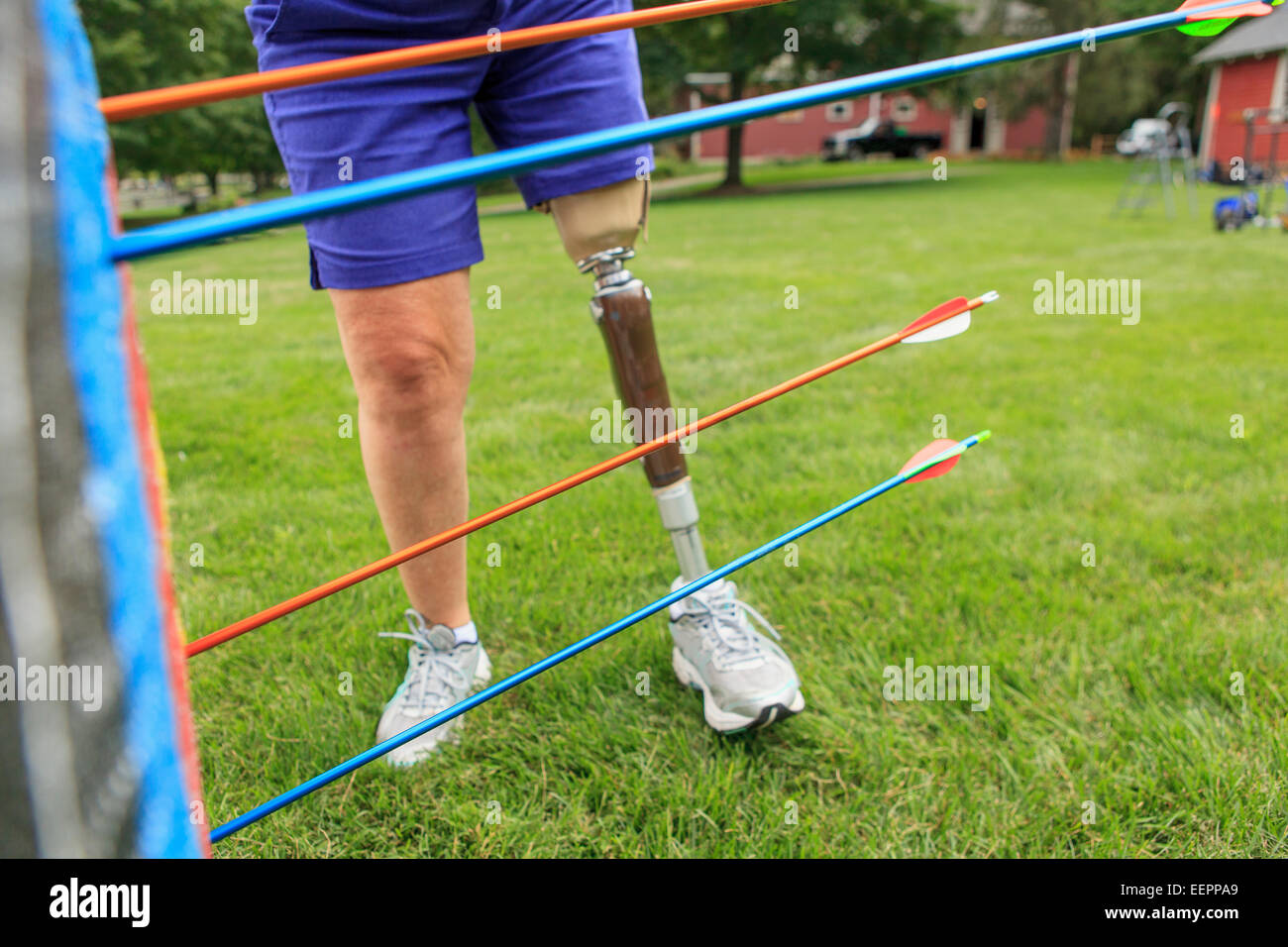 Donna con gamba protesico tirando le frecce dal bersaglio dopo la pratica di tiro con l'arco Foto Stock