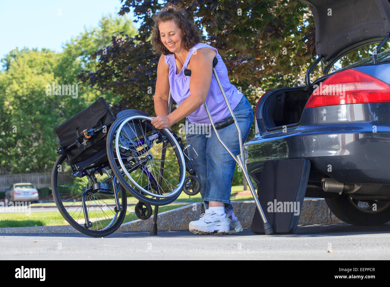 Donna con la Spina Bifida usando stampelle per mettere insieme sedia a rotelle dopo un viaggio in auto Foto Stock