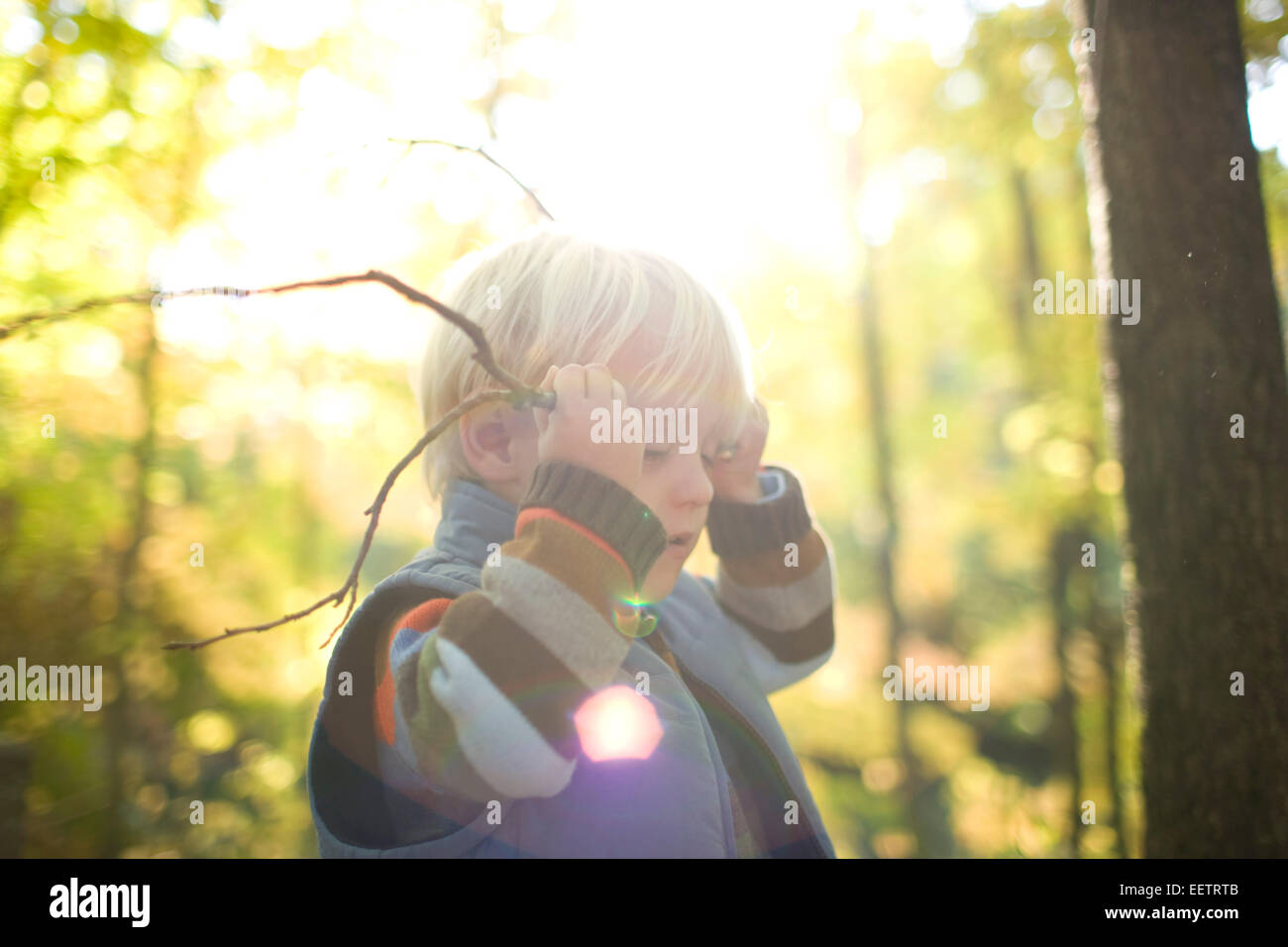 Giovane ragazzo giocando con i rami degli alberi, fingendo sono palchi. Foto Stock