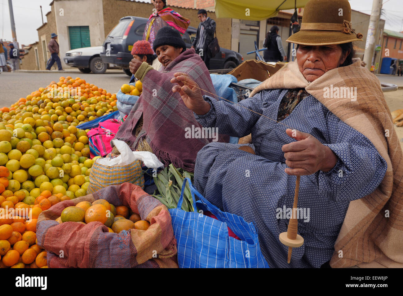Le donne indigene spin filato su mandrini mentre si lavora a una strada del mercato per la vendita di frutta di El Alto in Bolivia. Foto Stock