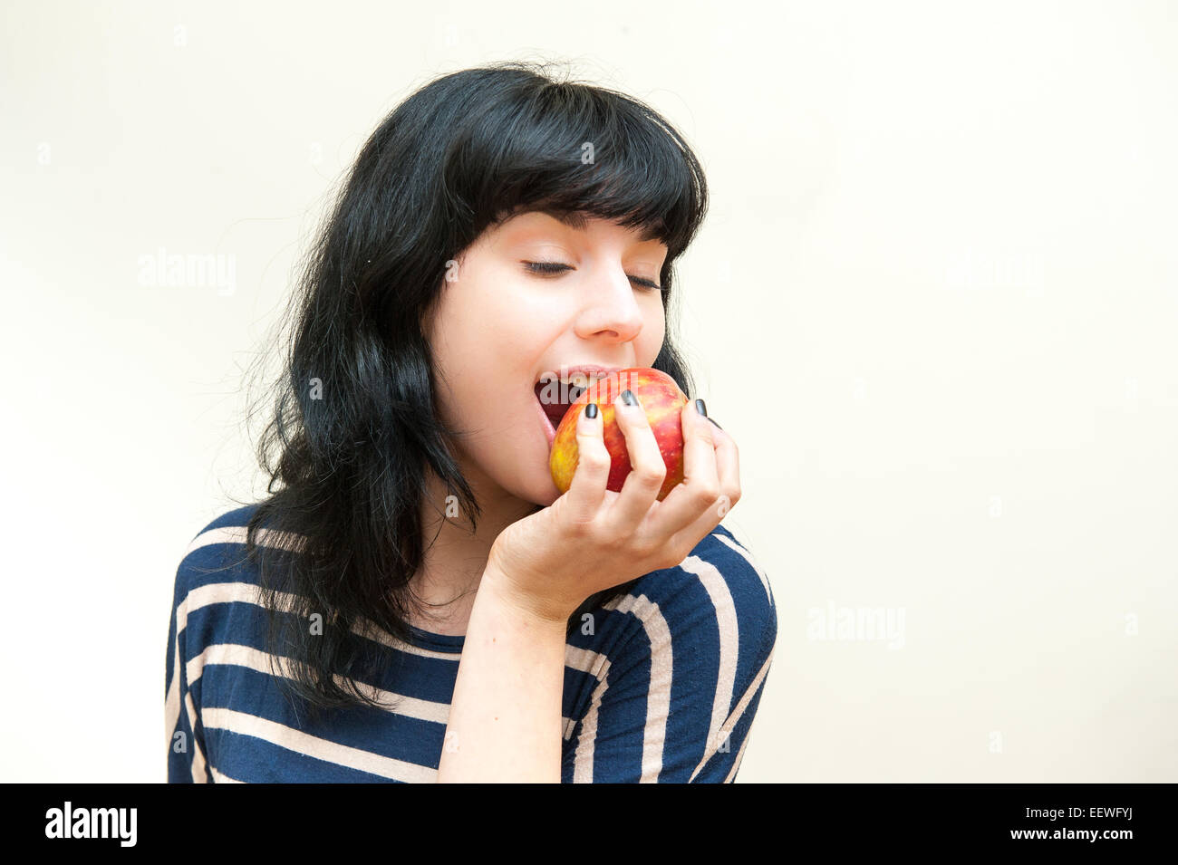 Bella bruna ragazza di mordere red apple con chiudere gli occhi su sfondo bianco Foto Stock